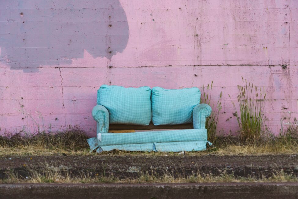 between the train tracks and a pink wall a broken blue sofa is pictured