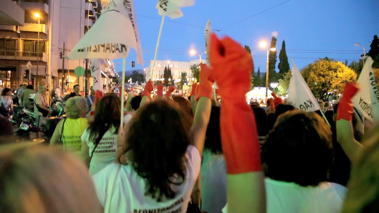 Στιγμιότυπο από τη διαδήλωση, διακρίνονται γυναίκες και η υψωμένη γροθιά ενός χεριού που φορά ένα κόκκινο πλαστικό γάντι καθαρισμού