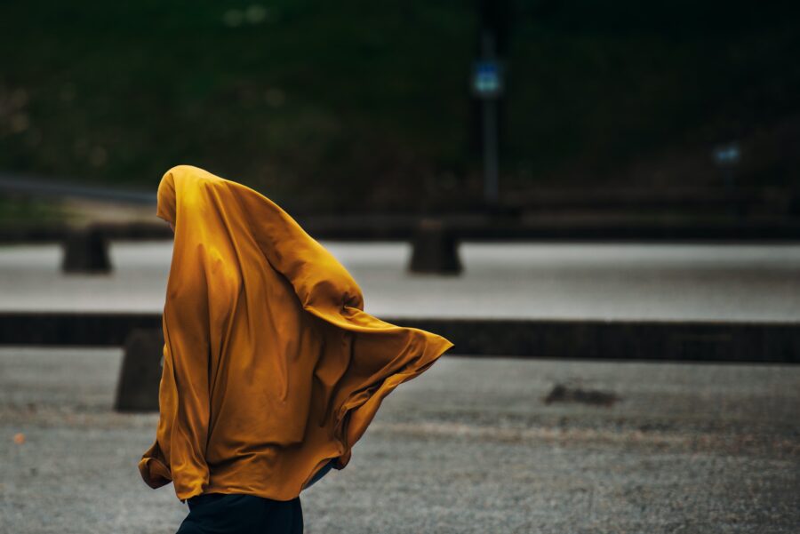 a woman in a long yellow scarf crosses the street