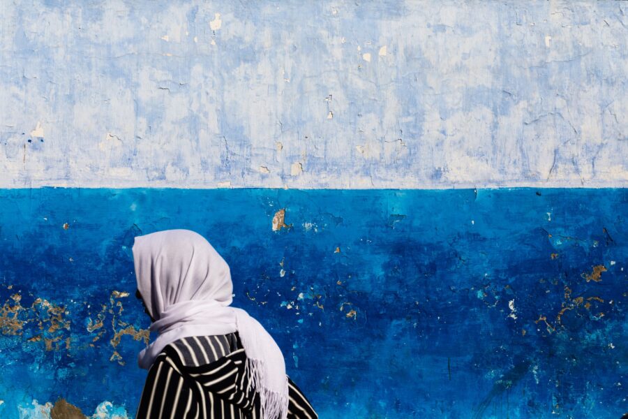 A woman with a hijab walks in front of a blue and off-white wall