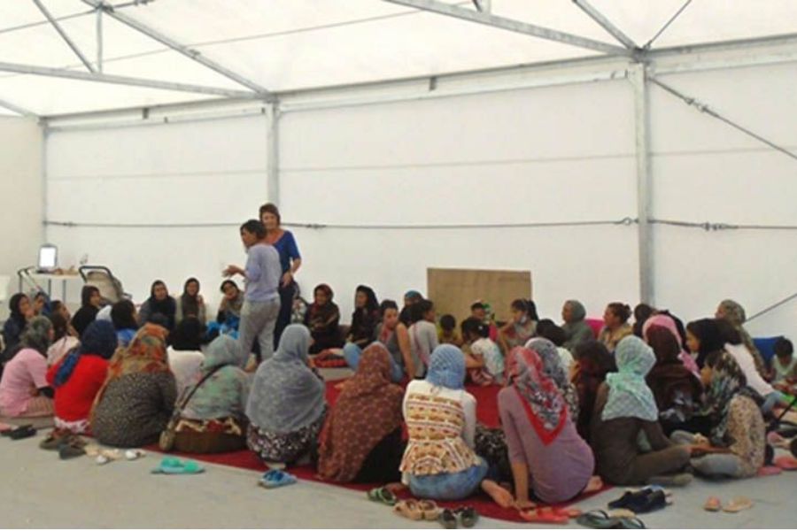 Photo of women inside a tend, sitting on the floor around two other women.