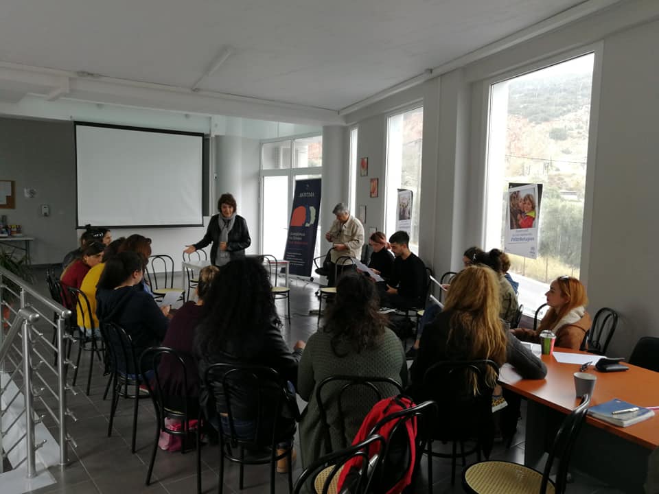 στιγμιότυπο από την επιμόρφωση, συμμετέχουσες/οντες κάθονται περιμετρικά μιας φωνεινής αίθουσας, η εισηγήτρια βρίσκεται όρθια στο κέντρο