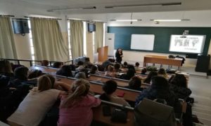 στιγμιότυπο από σεμινάριο, συμμετέχουσες/οντες σε αμφιθέατρο παρακολουθούν την εισηγήτρια