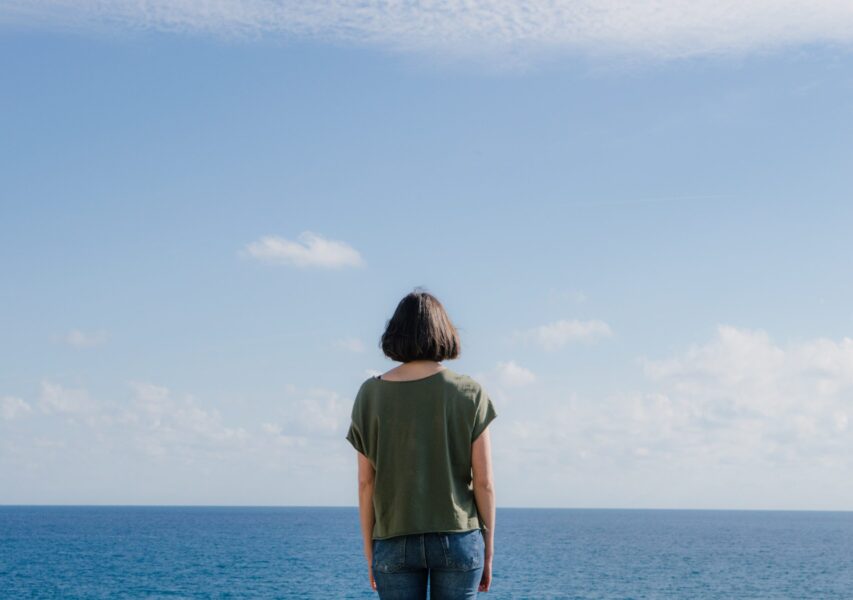 a woman with her back to the lens looking towards the sea