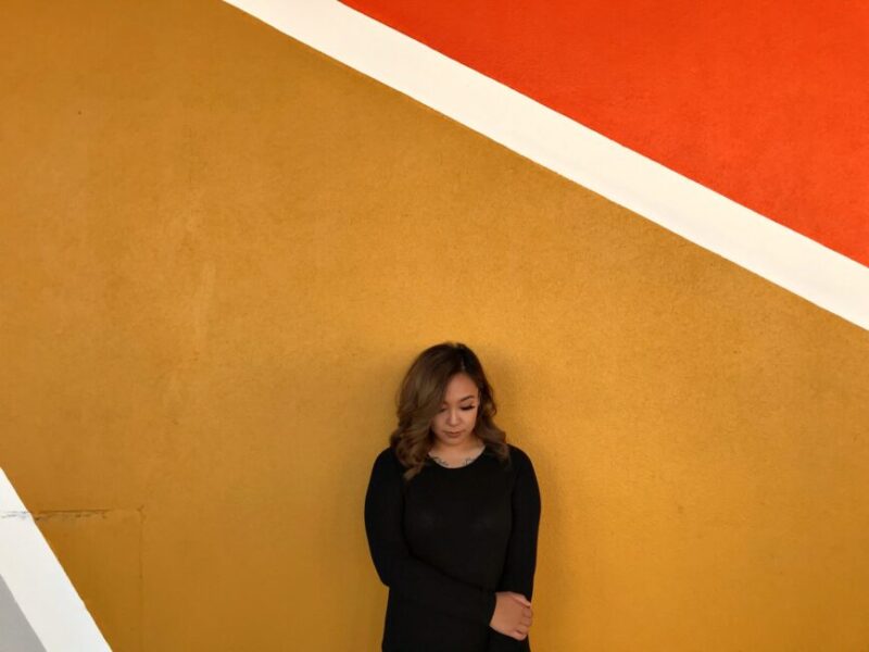 a woman stands with her back to a yellow-orange wall