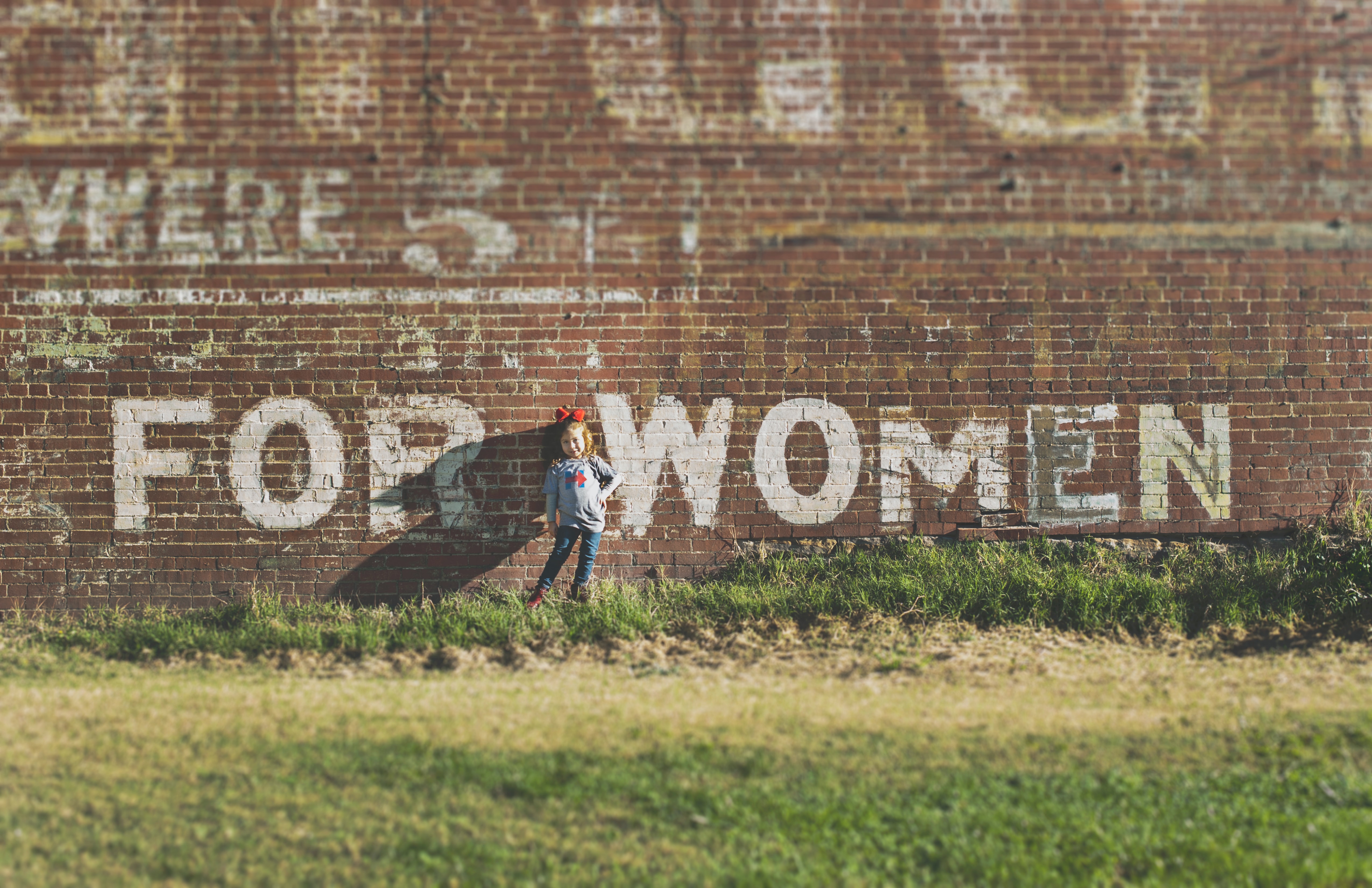 a girl resting on a wall of red bricks that writes "for women"