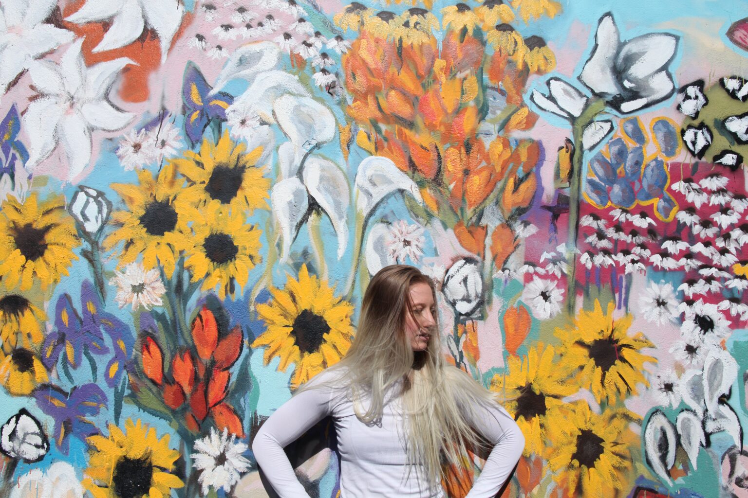 a woman stands with her back to a colorful wall with flower paintings