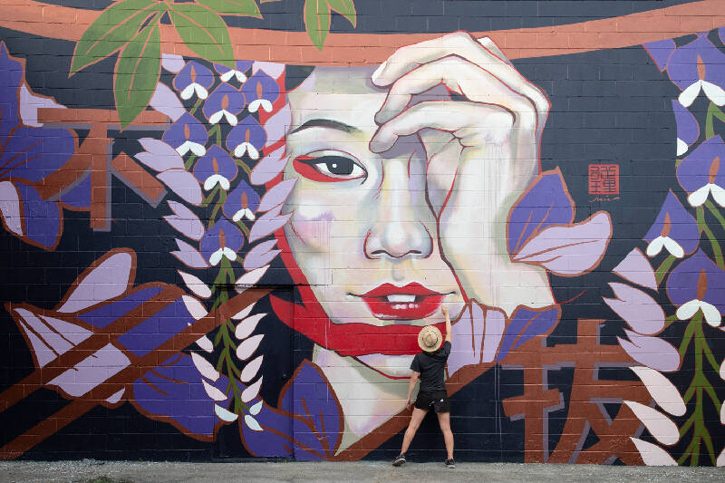 street artist finishes a graffiti that represents a female face of Asian aesthetics, around her are painted ideograms and flowers