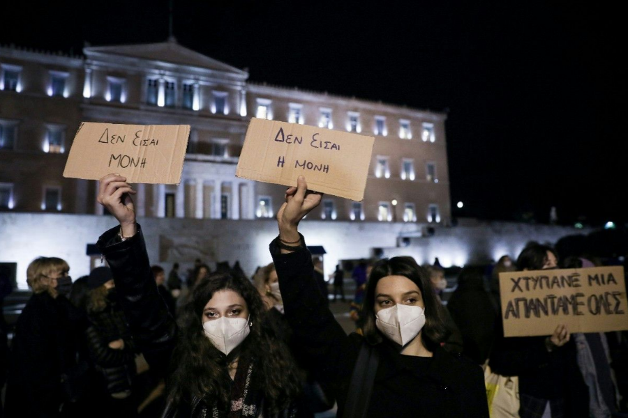 snapshot of a feminist demonstration in front of the parliament, two young women hold cardboards of the same size which they each hold up with their left hand, on one is written "You are not alone" on the other "You are not the only one"