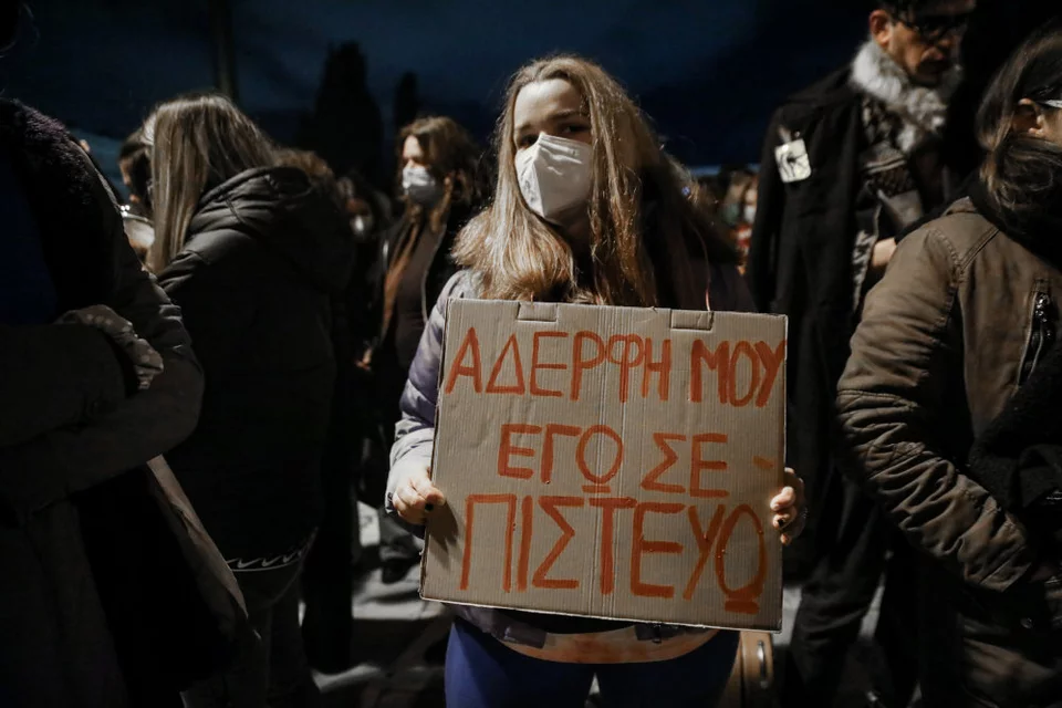 protest shot, a young woman holds a cardboard sign that reads 'My sister I believe you'