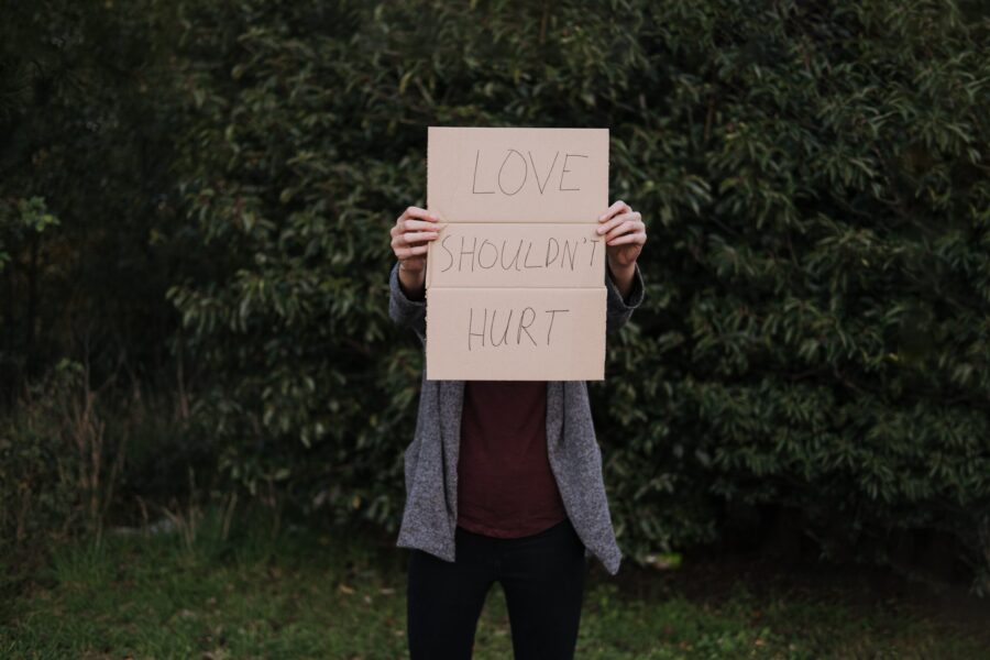 a woman is holding a cardboard that says "Love shouldn't hurt"