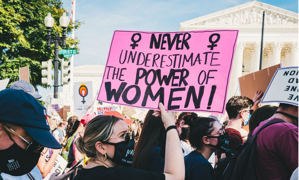 Photo. A banner in a protest which says "Never underestimate the power of women".