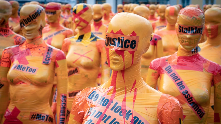 κούκλες βιτρίνας τυλιγμένες με κόκκινες ταινίες σήμανσης, πάνω σε αυτές γράφει με μαύρα γράμματα «justice» «#metoo» «stalking»