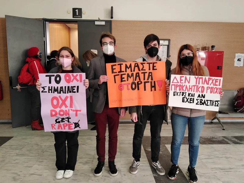 στιγμιότυπο από παρέμβαση έξω από δικαστική αίθουσα, δύο νέες και δύο νέοι κρατούν πικέτες, μία από αυτές γράφει «είμαστε γεμάτα (στ)οργή»