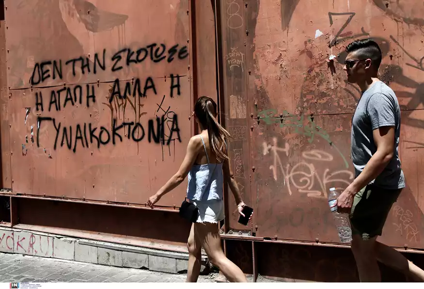 μια γυναίκα βαδίζει δίπλα σε έναν τοίχο που γράφει «Δεν τη σκότωσε η αγάπη αλλά η γυναικοκτονία»