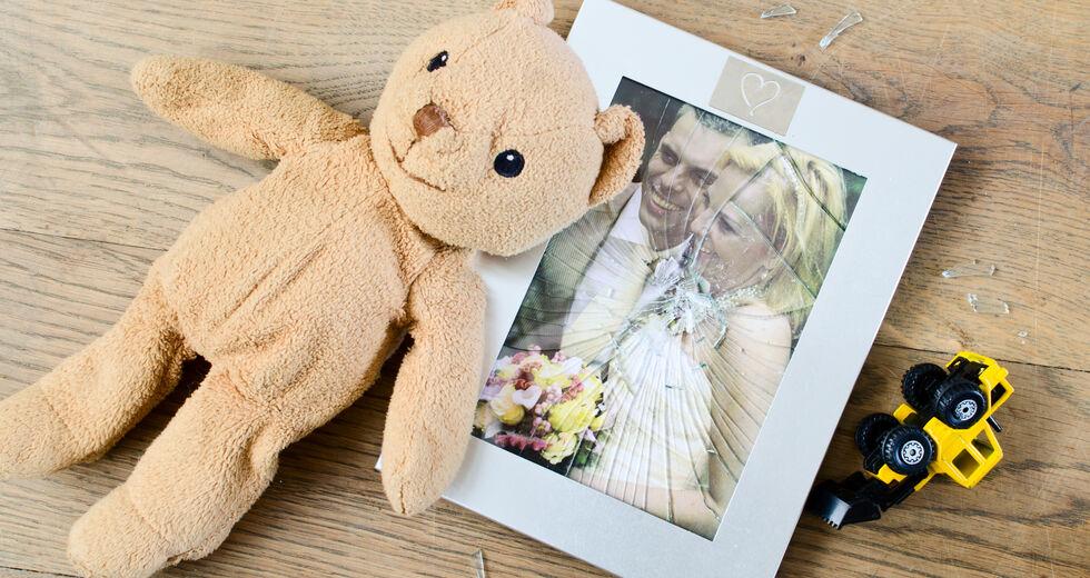 μια φωτογραφία γάμου πίσω από μια σπασμένη κορνίζα και δύο παιδικά παιχνίδια