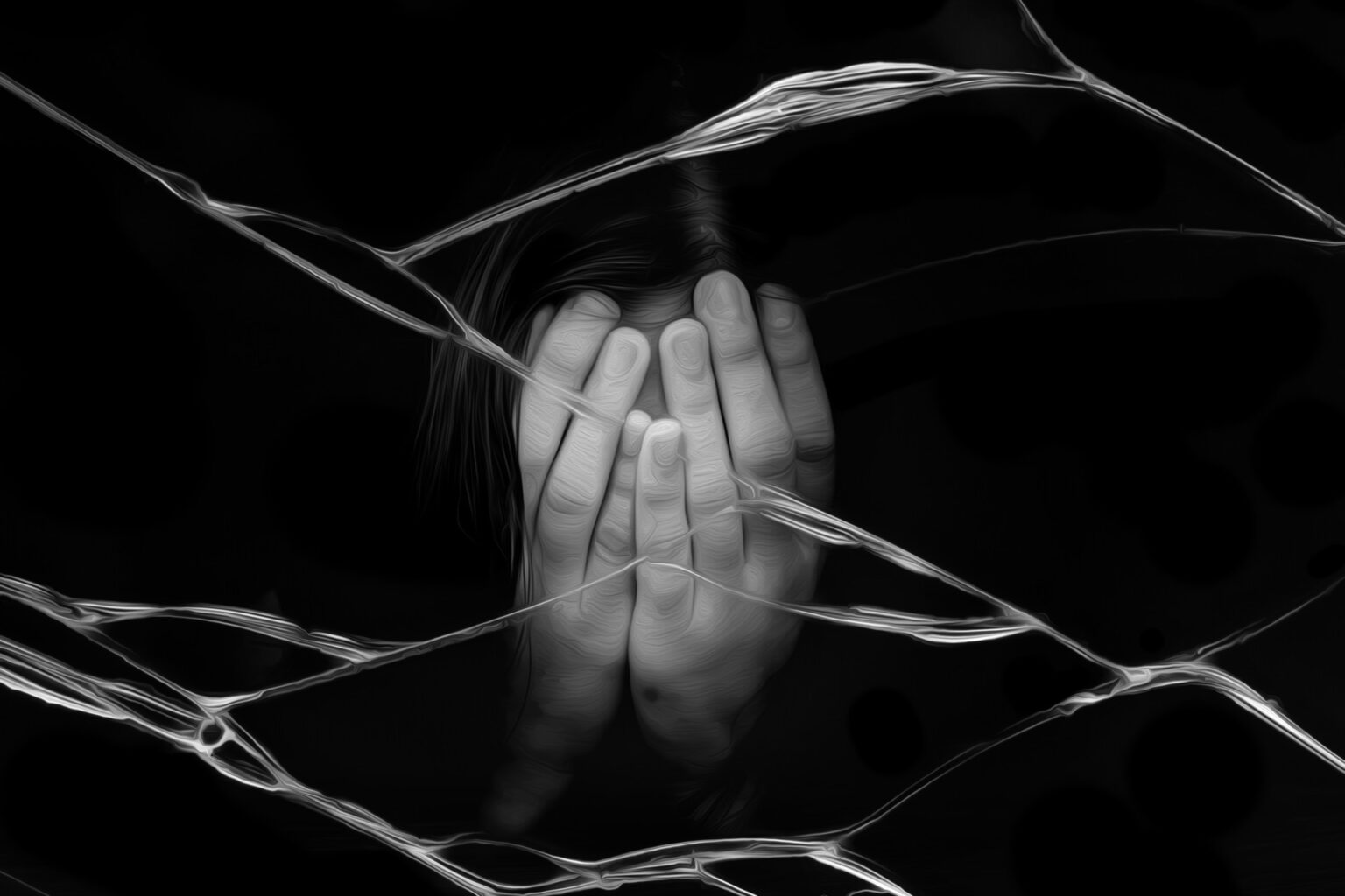 μια γυναίκα κρύβει το πρόσωπο της μέσα στις παλάμες της πίσω από ένα σπασμένο γυαλί