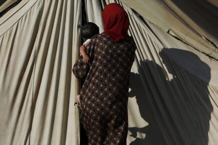 προσφύγισσα με ένα μωρό στην αγκαλιά μπροστά από την είσοδο σκηνής