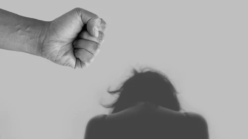 μια γυναικεία φιγούρα σκυφτή προς τα εμπρός, από πάνω της μία σφιγμένη ανδρική γροθιά