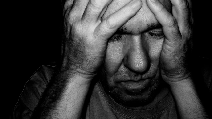 ένας άνδρας με κλειστά μάτια κρατά το κεφάλι του μέσα στις παλάμες του