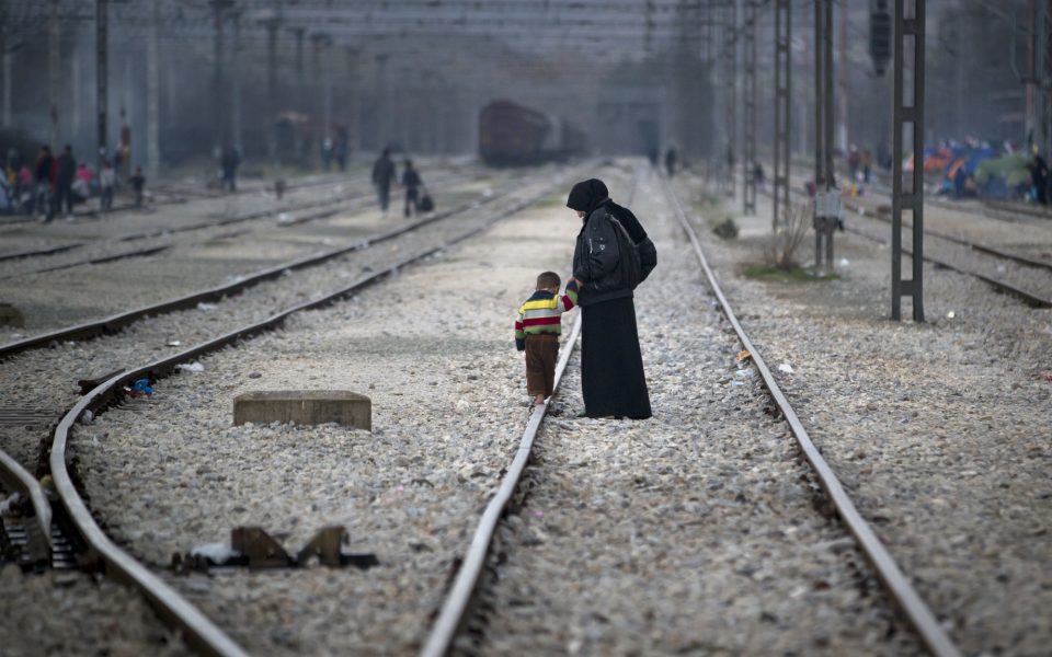 μια προσφύγισσα κρατά ένα παιδί από το χέρι και προχωρά πάνω στις ράγιες
