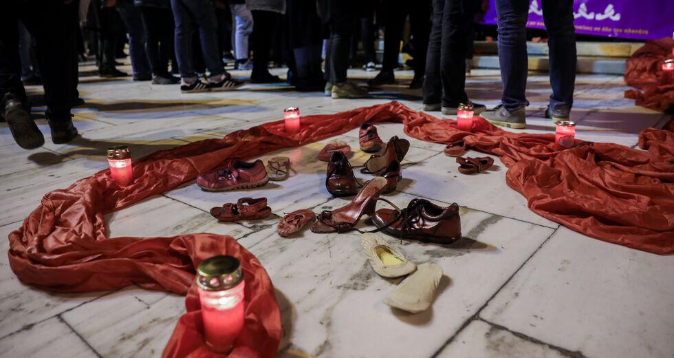 στιγμιότυπο από διαμαρτυρία για τις γυναικοκτονίες, στις πλάκες του δρόμου ένα κόκκινο πανί, αναμμένα κεριά και γυναικεία παπούτσια