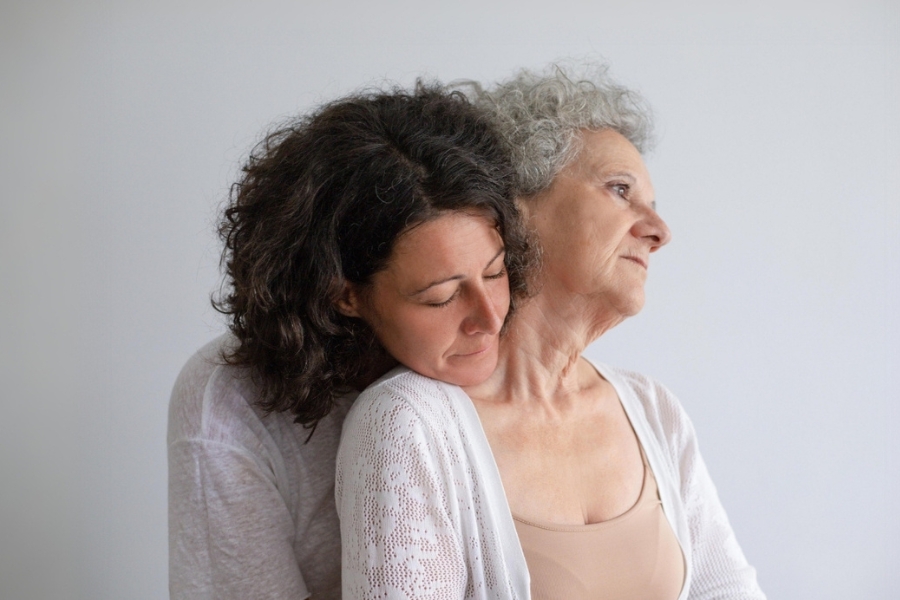 δύο γυναίκες μια νεότερη και μια μεγαλύτερη με γκρίζα κοντά μαλλιά. η νεότερη αγκαλιάζει τη μεγαλύτερη