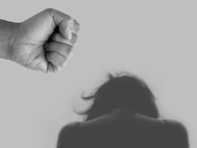 μια γυναικεία φιγούρα σκυφτή προς τα εμπρός, από πάνω της μία σφιγμένη ανδρική γροθιά