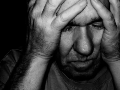 ένας άνδρας με κλειστά μάτια κρατά το κεφάλι του μέσα στις παλάμες του