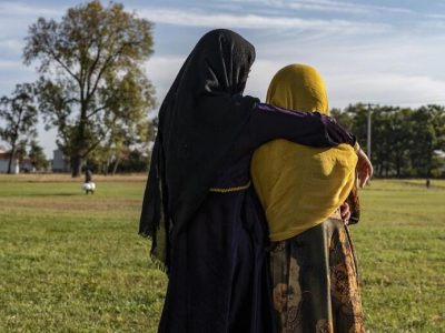 μια ψηλόλιγνη προσφύγισσα με μαύρη μαντίλα αγκαλιάζει μια άλλη με κίτρινη μαντίλα