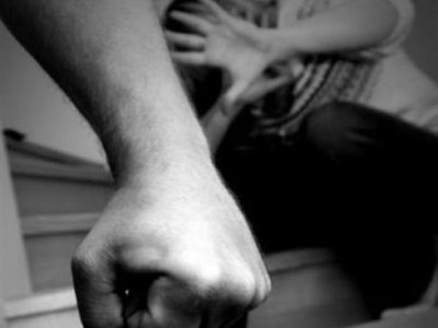 η σφιγμένη γροθιά ενός άνδρα και στο φόντο μια γυναίκα που κρύβεται πίση από την ανοιχτή της παλάμη