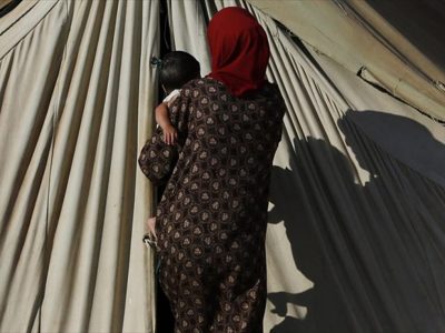 προσφύγισσα με ένα μωρό στην αγκαλιά μπροστά από την είσοδο σκηνής