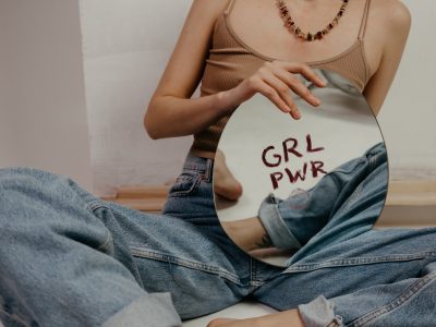μια γυναίκα κάθεται οκλαδόν και κρατά έναν καθρέφτη που γράφει «GRL PWR»
